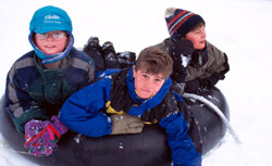 Three boys riding a tube down a snowy slope