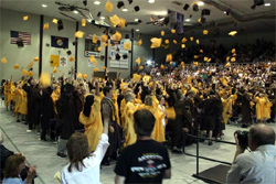 Auditorium full of graduares tossing their caps into the air.