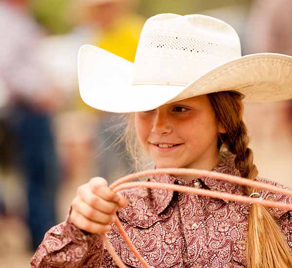 Young blonde girl in a cowboy hat winding a rope.